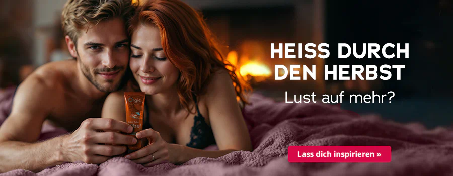Paar liegt eng umschlungen auf rosa Bettdecke, hält ein Massageöl in der Hand; Kaminfeuer im Hintergrund, Text „Heiss durch den Herbst – Lust auf mehr?“ und Button „Lass dich inspirieren“