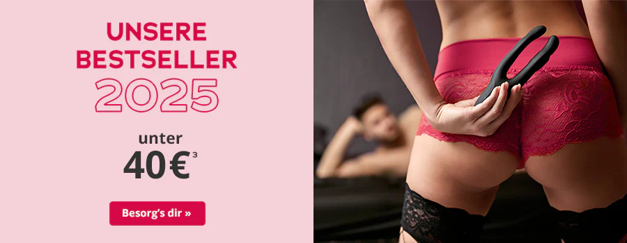 Frau in roter Spitzenunterwäsche hält ein schwarzes Toy hinter dem Rücken, im Hintergrund liegt ein Mann auf einem Bett. Text: 'Unsere Bestseller 2025 – unter 40 €'. CTA: 'Besorg’s dir'