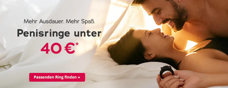 Ein lächelndes Paar liegt eng beieinander im Bett und schaut sich an. Die Frau hält einen schwarzen Penisring in der Hand. Links steht der Text „Mehr Ausdauer. Mehr Spaß. Penisringe unter 40 €*“ mit rotem Button „Passenden Ring finden ».
