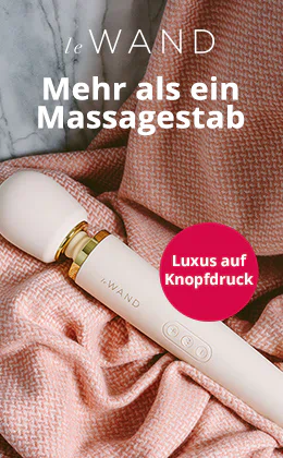 Ein weißer Massage-Stab der Marke le WAND liegt auf roséfarbenem Strickstoff vor grauer Marmorfläche. Oben steht „Mehr als ein Massagestab“, rechts „Luxus auf Knopfdruck“. Unten befindet sich ein roter Button „Jetzt entdecken“.
